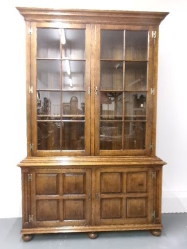 A large two-section warm brown oak bookcase featuring two upper glazed doors with internal shelves above two lower field-panelled wooden doors. View VIII