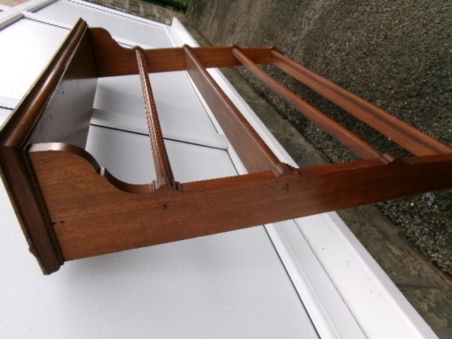 A mahogany wall-hanging rack featuring a top shelf, open tiers with horizontal retaining bars, shaped side brackets, and top brass mounting rings. View VI