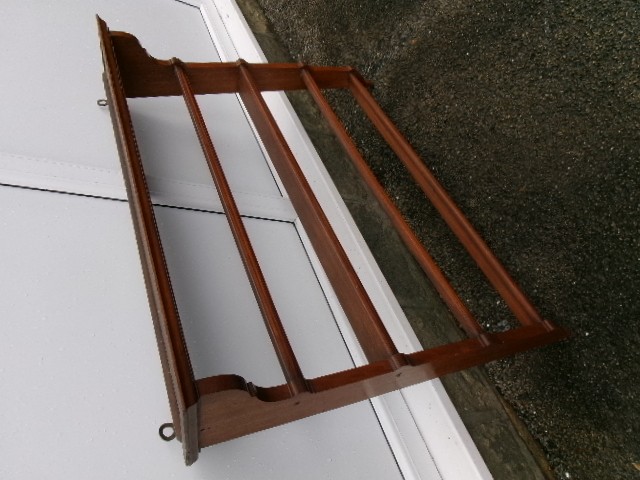 A mahogany wall-hanging rack featuring a top shelf, open tiers with horizontal retaining bars, shaped side brackets, and top brass mounting rings. View VII
