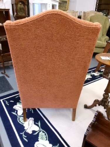 A high-backed Georgian style wing armchair with rolled arms, upholstered in textured orange fabric, accompanied by a matching square footstool. View V
