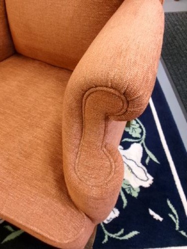 A high-backed Georgian style wing armchair with rolled arms, upholstered in textured orange fabric, accompanied by a matching square footstool. View VII