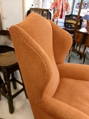 A high-backed Georgian style wing armchair with rolled arms, upholstered in textured orange fabric, accompanied by a matching square footstool. View X