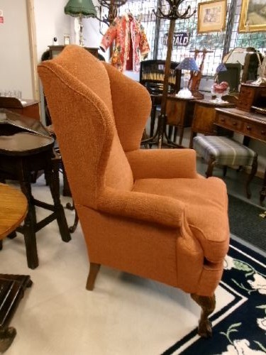 A high-backed Georgian style wing armchair with rolled arms, upholstered in textured orange fabric, accompanied by a matching square footstool. View IX