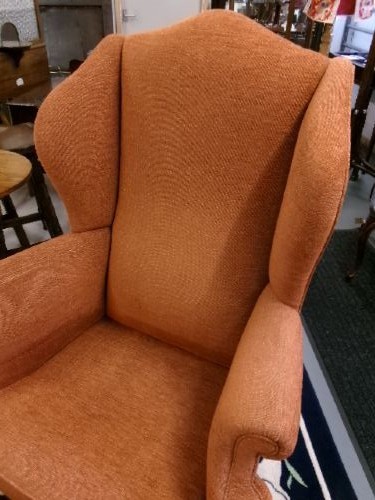 A high-backed Georgian style wing armchair with rolled arms, upholstered in textured orange fabric, accompanied by a matching square footstool. View VIII