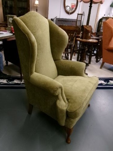 A high-backed Georgian style wing armchair upholstered in textured olive green fabric with dark wooden legs.