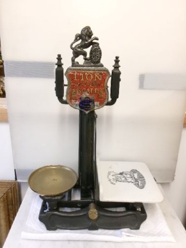 A Victorian cast iron and brass commercial weighing scale featuring a top lion crest, brass pan, and ceramic platform.