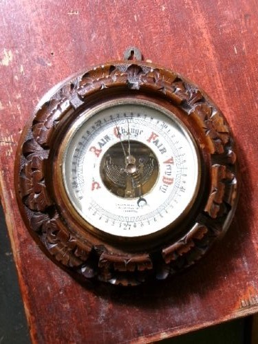 A circular Edwardian aneroid barometer set within a hand-carved mahogany frame with a brass bezel and visible mechanical movement. View VII