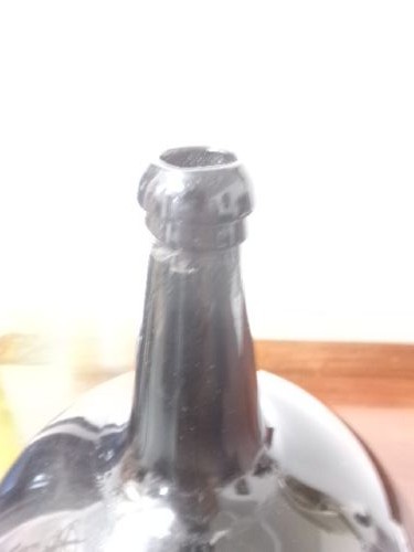 A dark green hand-blown glass onion bottle featuring a broad bulbous body, a long tapered neck, and an applied glass string rim. View II