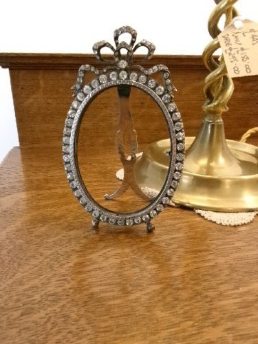 A small silver-plated oval easel picture frame decorated with clear paste stones and topped with a ribbon bow motif. View III