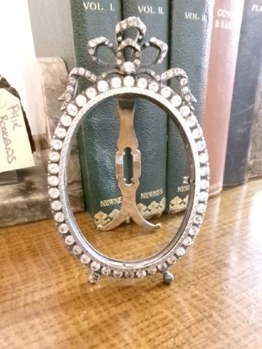 A small silver-plated oval easel picture frame decorated with clear paste stones and topped with a ribbon bow motif. View V