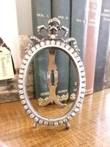 A small silver-plated oval easel picture frame decorated with clear paste stones and topped with a ribbon bow motif. View VI