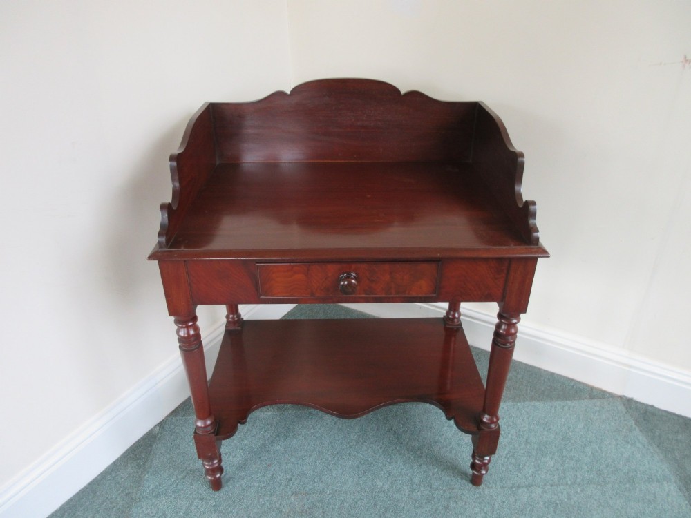 A Victorian mahogany night stand featuring a shaped gallery splashback, a single frieze drawer with a wooden knob, an open lower undertier, and turned legs.