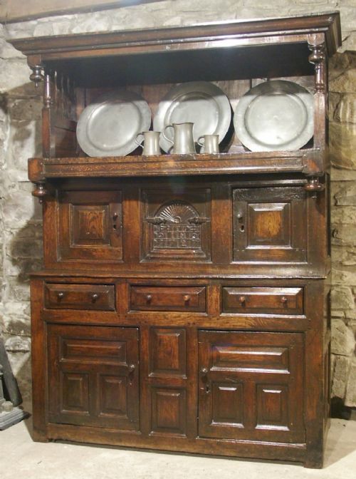 fig 1. An eighteenth-century dark oak Welsh cwpwrdd tridarn featuring three tiered sections, carved date detailing, fielded panels, and turned pillars.