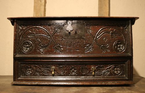 fig 1. A 17th-century dark oak carved table box featuring scrollwork leaf motifs, carved initials HC, an iron lockplate, and a lower drawer.
