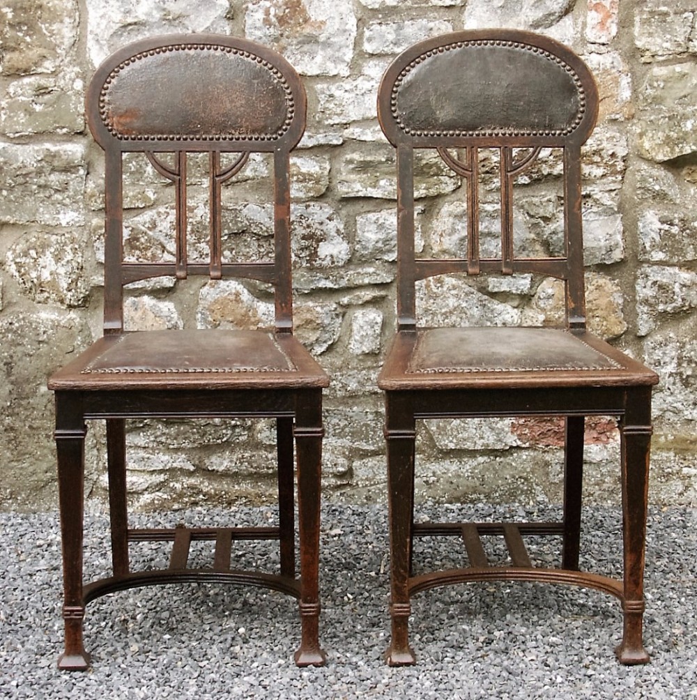 A pair of dark oak Art Nouveau side chairs with leather padded backs and seats secured with metal studs.