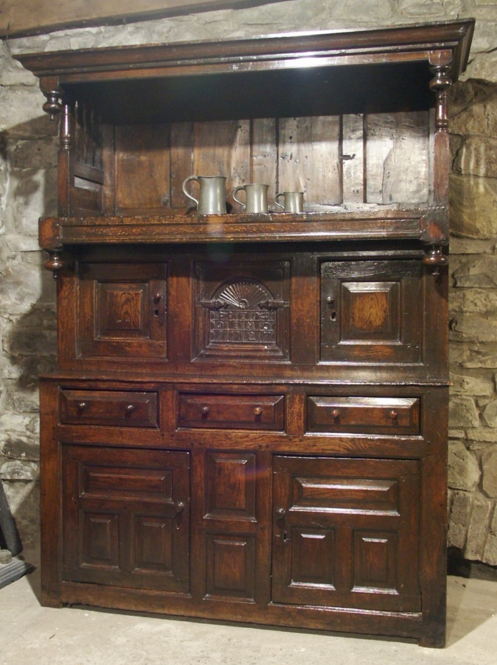 An eighteenth-century dark oak Welsh cwpwrdd tridarn featuring three tiered sections, carved date detailing, fielded panels, and turned pillars.