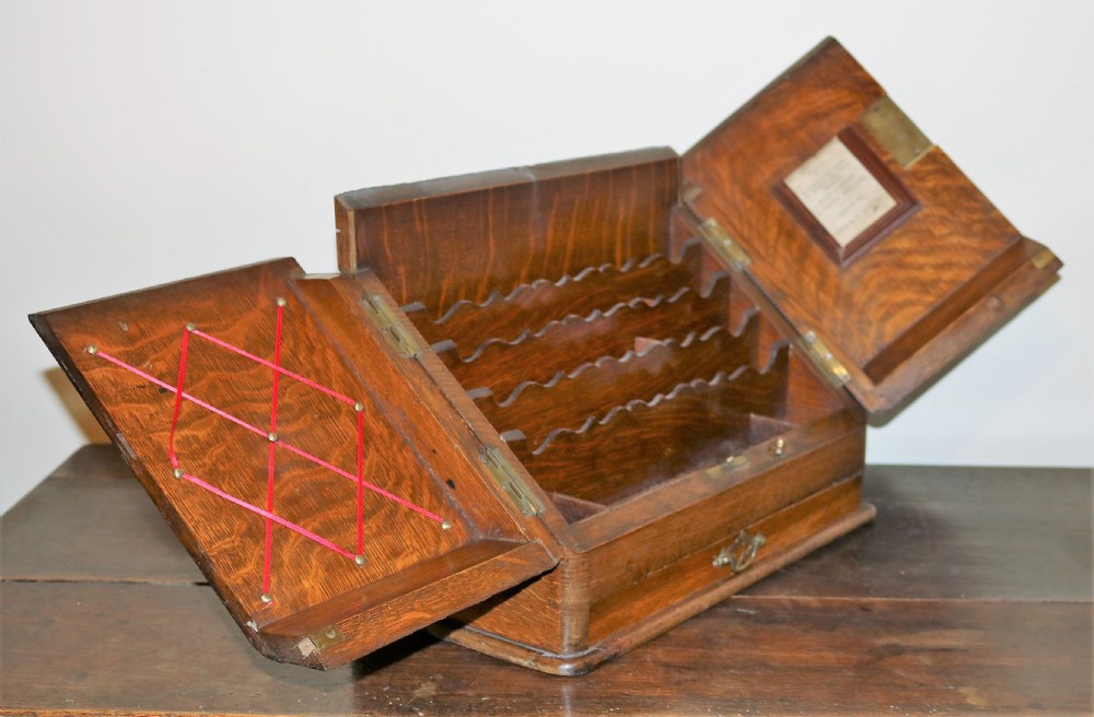 An open oak desktop stationery cabinet featuring tiered scalloped letter dividers, two hinged doors with ribbon memo webbing and frame fittings, and a single lower drawer. View II