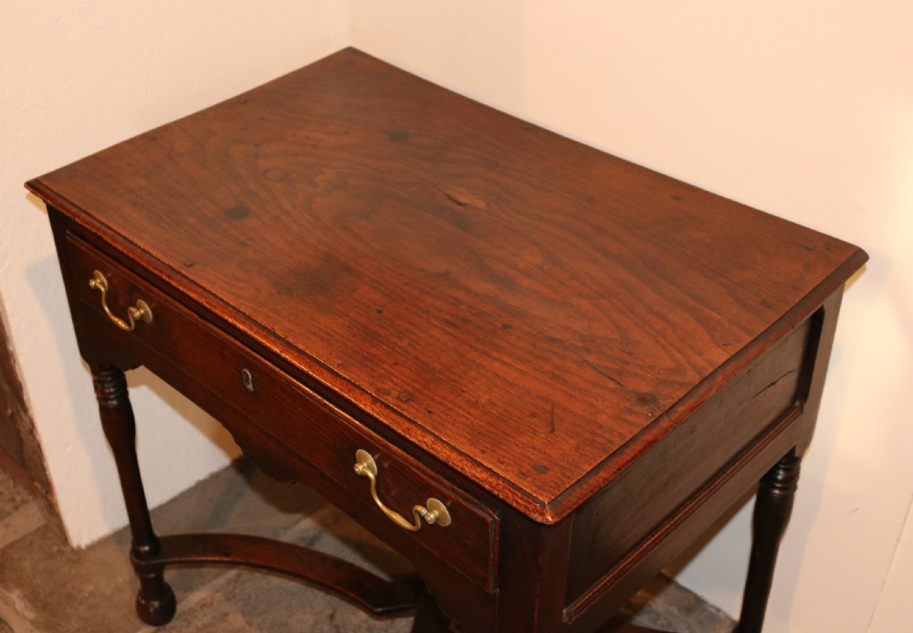 An 18th-century dark oak side table featuring a single drawer with brass drop handles, a shaped apron, turned legs, and an X-frame stretcher. View IX