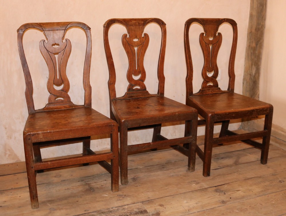 A set of three 18th-century Welsh elm side chairs featuring shaped splat backs, solid wooden seats, and square legs with stretchers.