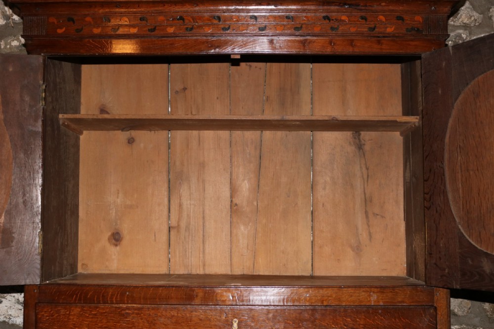 A Georgian Welsh oak secretaire press cupboard featuring upper doors with inlaid oval panels, a drop-front fitted writing section, and three lower drawers with oval brass handles. View VI