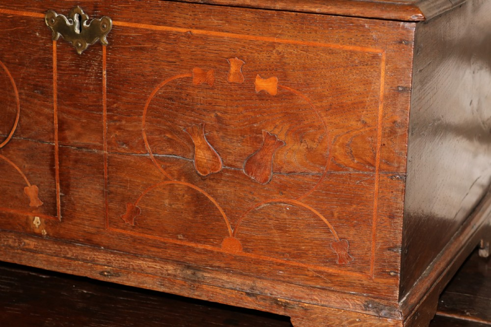 An 18th-century Welsh dark oak coffer bach featuring inlaid decorative scrolls on the front panel, bracket feet, and a central brass keyhole escutcheon. View VI