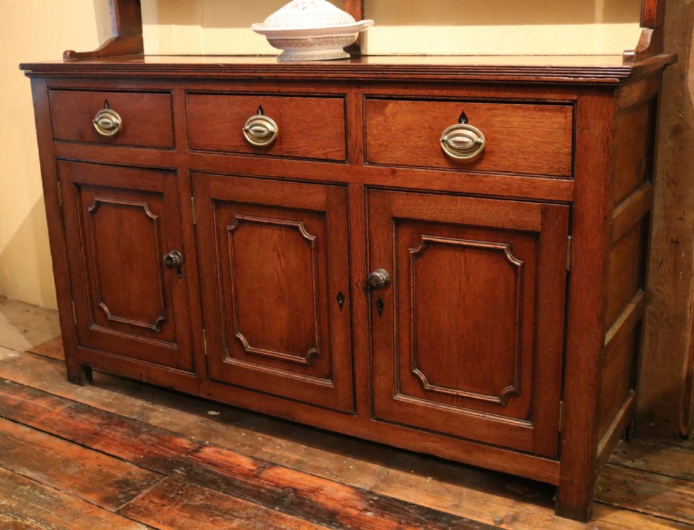 A late 18th-century Georgian Welsh oak dresser featuring a three-shelf open plate rack with brass hooks atop a cupboard base with three drawers and three panelled doors. View II