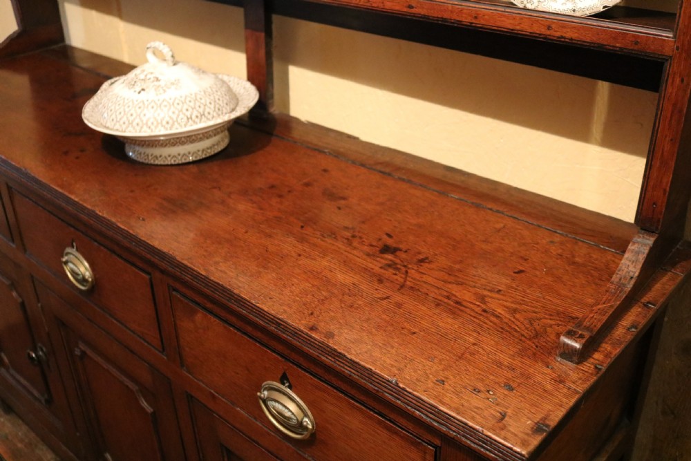 A late 18th-century Georgian Welsh oak dresser featuring a three-shelf open plate rack with brass hooks atop a cupboard base with three drawers and three panelled doors. View V
