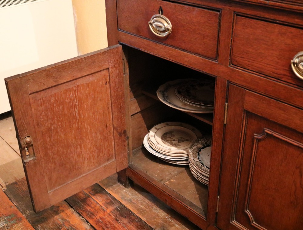 A late 18th-century Georgian Welsh oak dresser featuring a three-shelf open plate rack with brass hooks atop a cupboard base with three drawers and three panelled doors. View VI