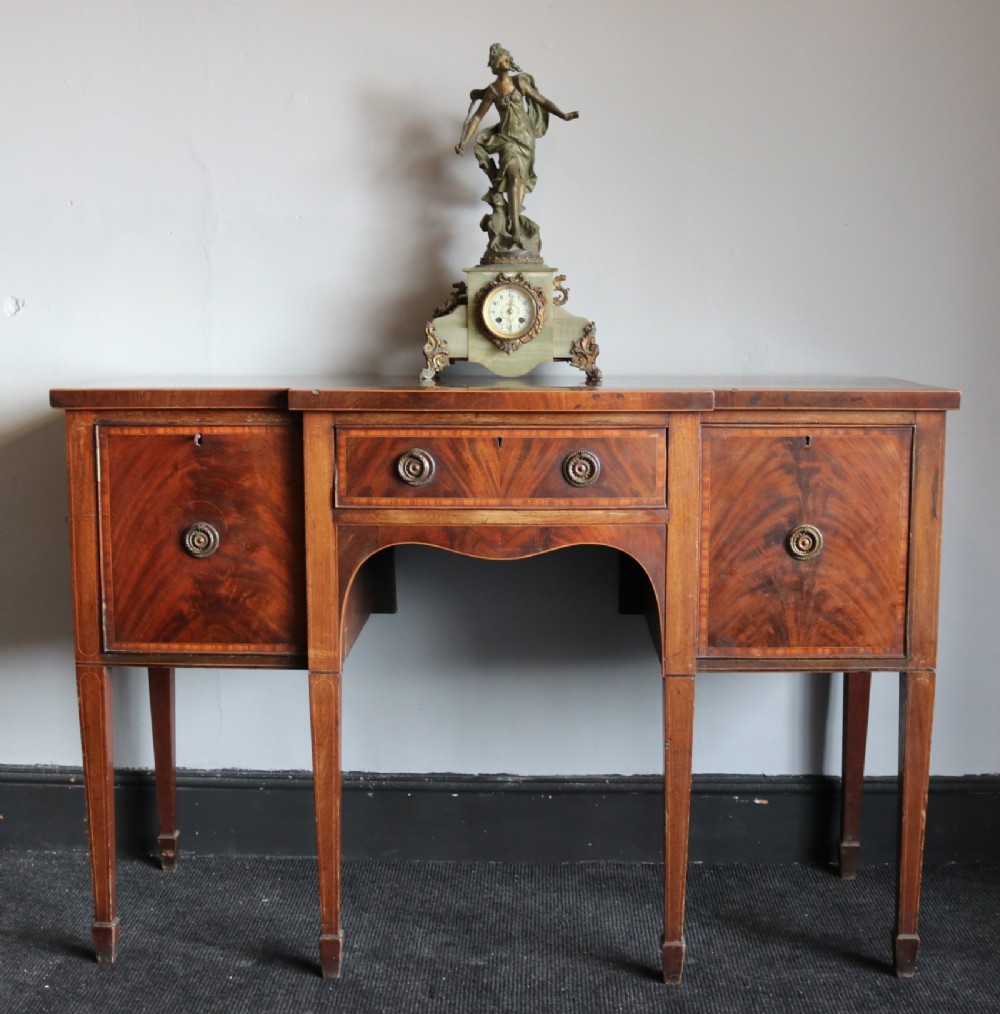 A late 18th-century Sheraton-style mahogany sideboard featuring flame veneer cupboards, a central drawer, an arched apron, and slender tapered legs.