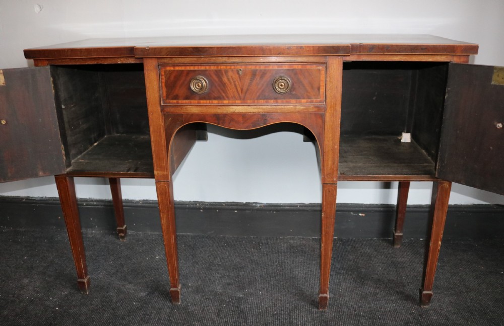 A late 18th-century Sheraton-style mahogany sideboard featuring flame veneer cupboards, a central drawer, an arched apron, and slender tapered legs. View V