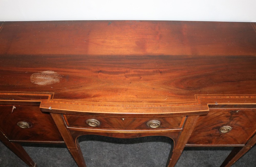 A late 18th-century Sheraton-style mahogany sideboard featuring flame veneer cupboards, a central drawer, an arched apron, and slender tapered legs. View VI