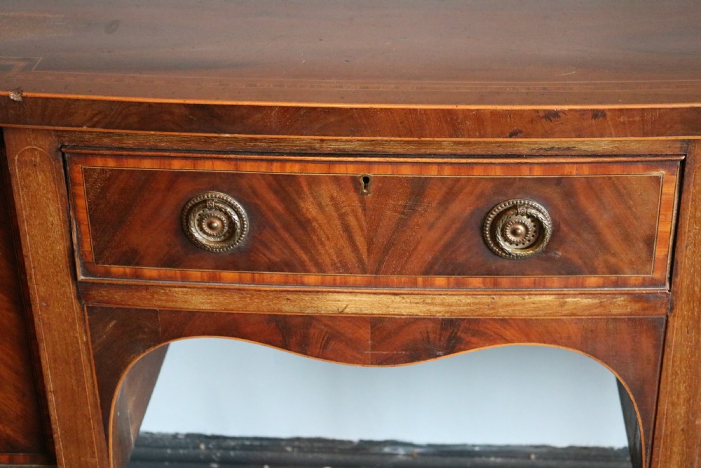 A late 18th-century Sheraton-style mahogany sideboard featuring flame veneer cupboards, a central drawer, an arched apron, and slender tapered legs. View VII