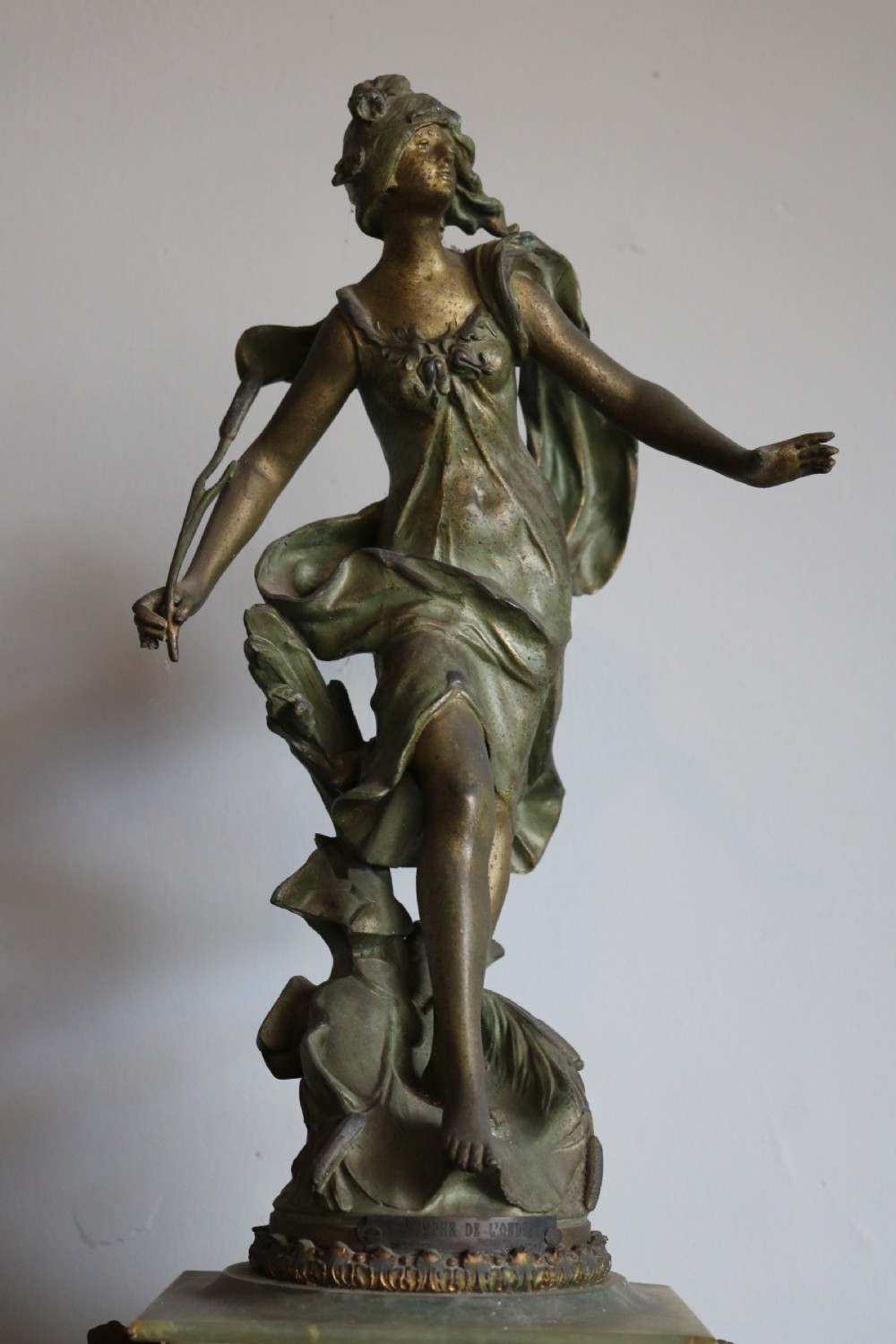 An Art Nouveau French mantel clock featuring a bronzed female figure standing atop a light green onyx base with ornate brass feet and a decorated circular dial. View III