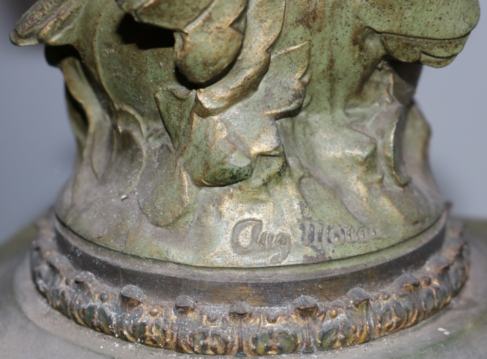 An Art Nouveau French mantel clock featuring a bronzed female figure standing atop a light green onyx base with ornate brass feet and a decorated circular dial. View IX