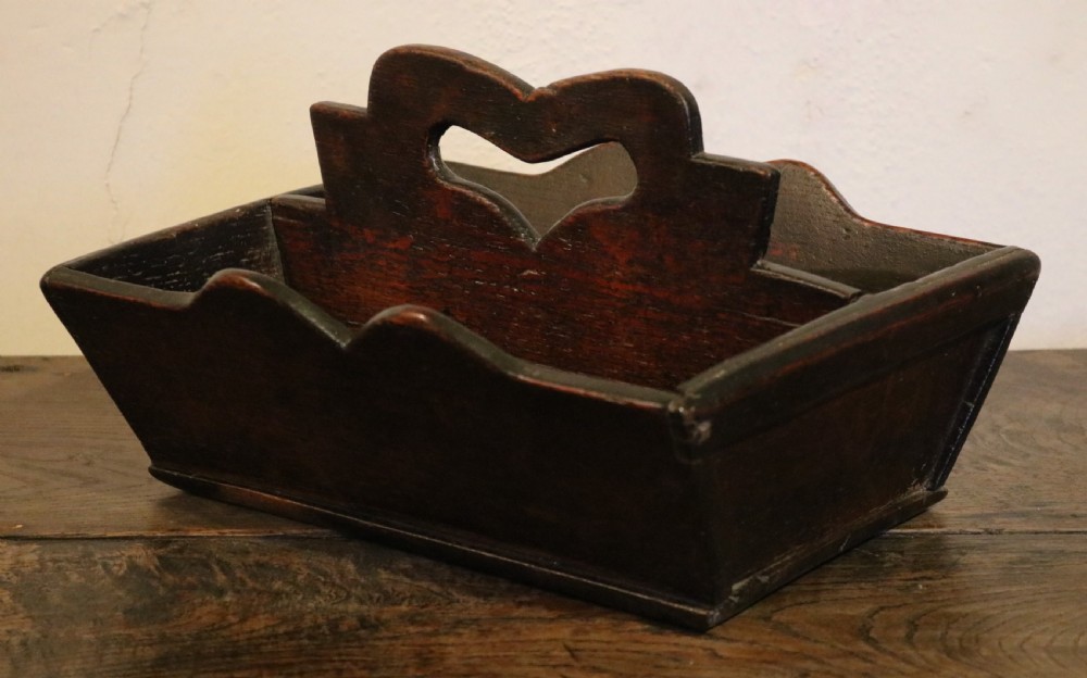 A dark oak 18th-century cutlery tray featuring a central divider with a carved heart-shaped handle aperture and scalloped sides.