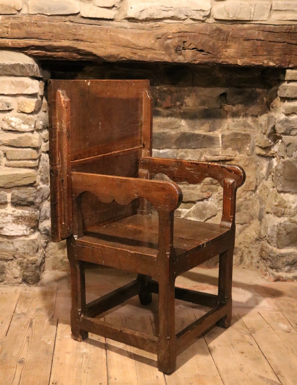 A 17th-century Welsh dark oak chair-table shown with its rectangular wooden top locked upright to form a backrest above shaped armrests and a square seat.