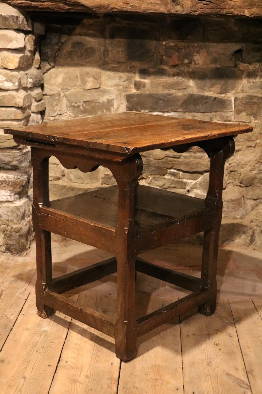 A 17th-century Welsh dark oak chair-table shown with its rectangular wooden top locked upright to form a backrest above shaped armrests and a square seat. View II
