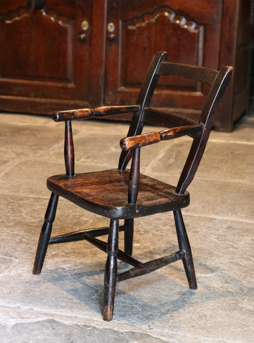 A nineteenth-century dark-stained Welsh childs primitive Windsor armchair featuring a thick slab seat, turned arms, and splayed legs. View II
