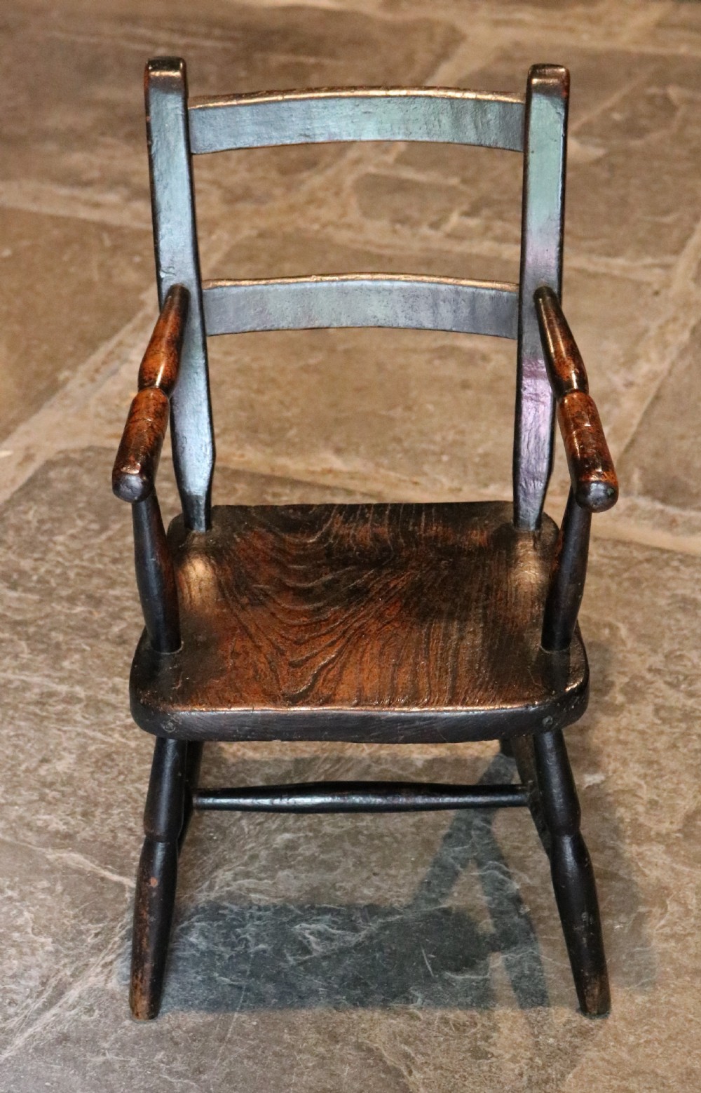 A nineteenth-century dark-stained Welsh childs primitive Windsor armchair featuring a thick slab seat, turned arms, and splayed legs. View III