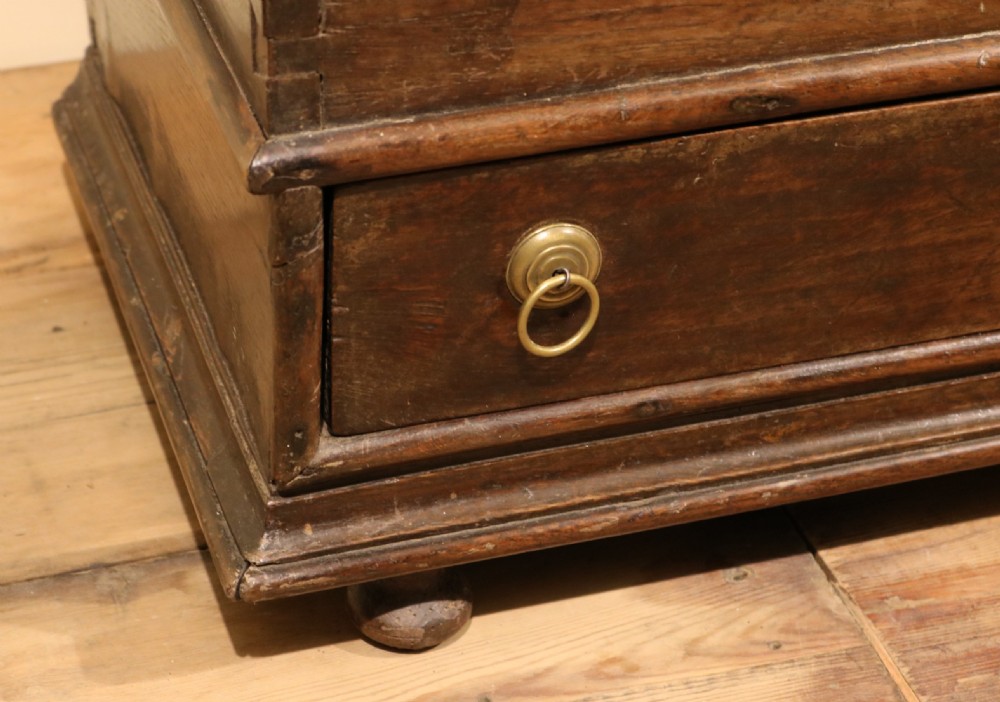A small 17th-century Welsh dark oak coffer bach featuring a hinged top, single lower drawer with brass ring handles, and turned bun feet. View VII