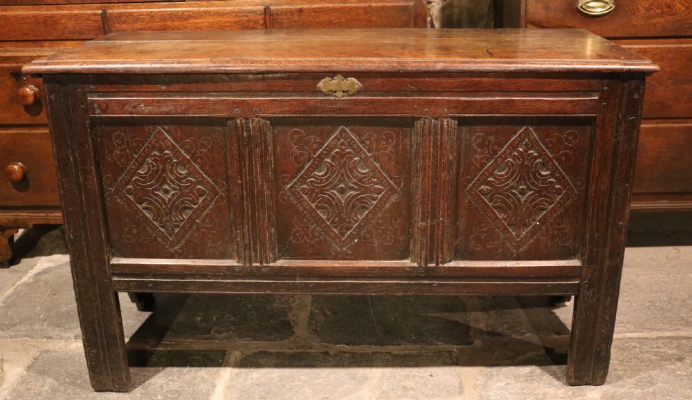 A seventeenth-century dark oak coffer featuring three carved front panels with geometric diamond lozenge motifs and a brass keyhole escutcheon. View VII