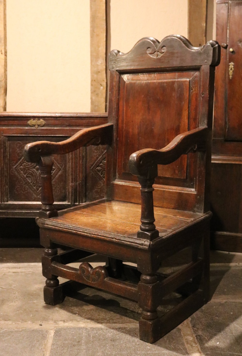 A 17th-century Welsh oak armchair featuring a central yew-wood back panel, down-swept armrests, turned front legs, and a carved crest rail.