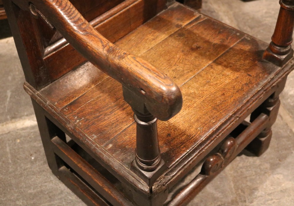 A 17th-century Welsh oak armchair featuring a central yew-wood back panel, down-swept armrests, turned front legs, and a carved crest rail. View X