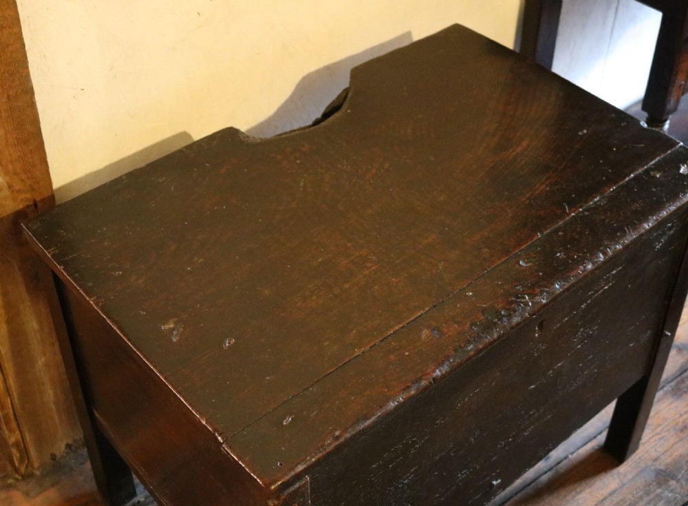 A dark brown primitive oak coffer featuring a hinged lid, straight legs, and a small central iron keyhole. View V