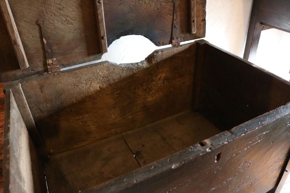 A dark brown primitive oak coffer featuring a hinged lid, straight legs, and a small central iron keyhole. View VI