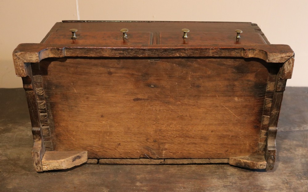 An 18th-century dark oak miniature bureau featuring a sloped lid, a circular brass keyhole escutcheon, and two small drawers at the base with brass knob handles. View VIII