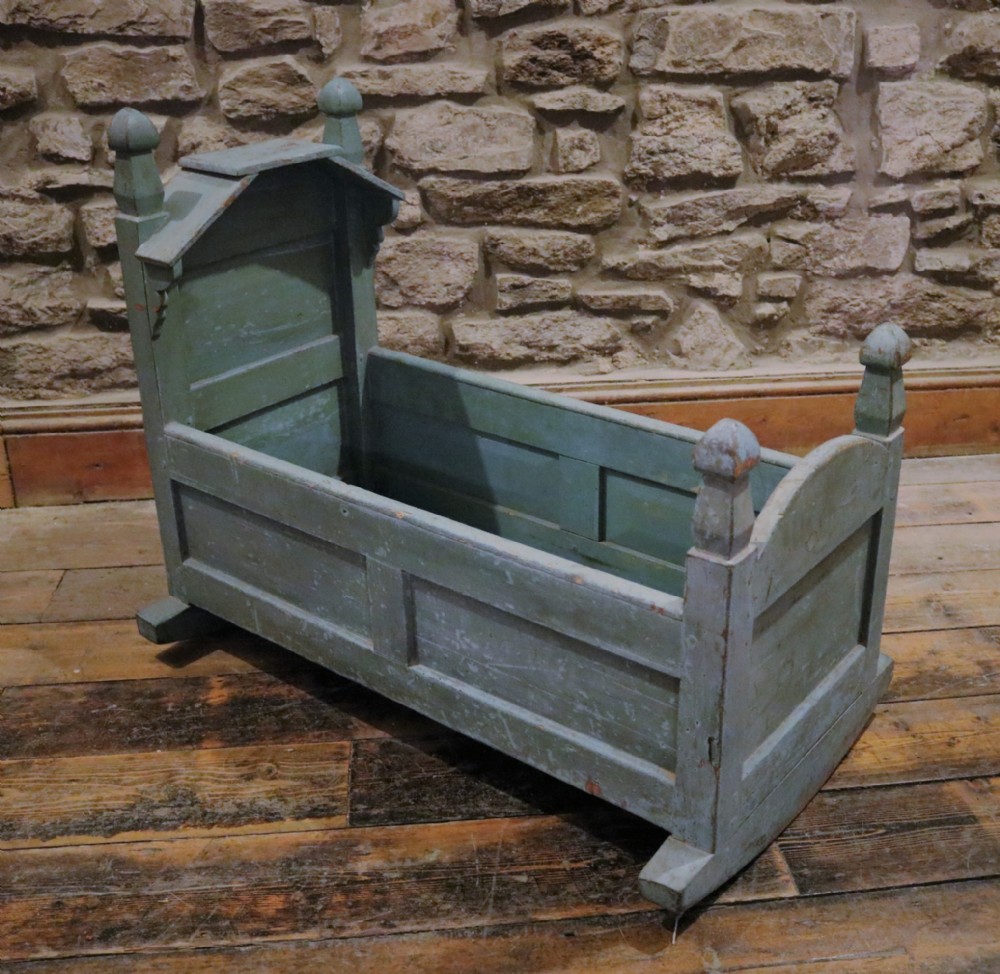 An antique Welsh pine hooded rocking cradle with original distressed blue paint, panelled sides, turned corner finials, and wooden rockers.