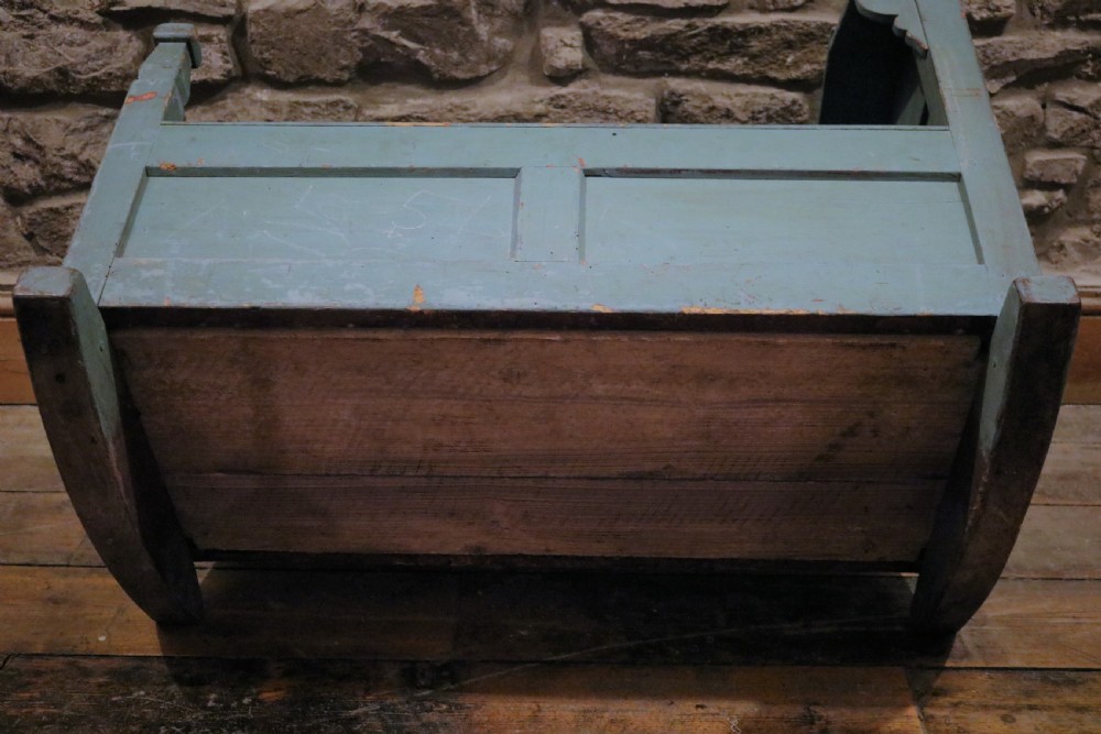An antique Welsh pine hooded rocking cradle with original distressed blue paint, panelled sides, turned corner finials, and wooden rockers. View X