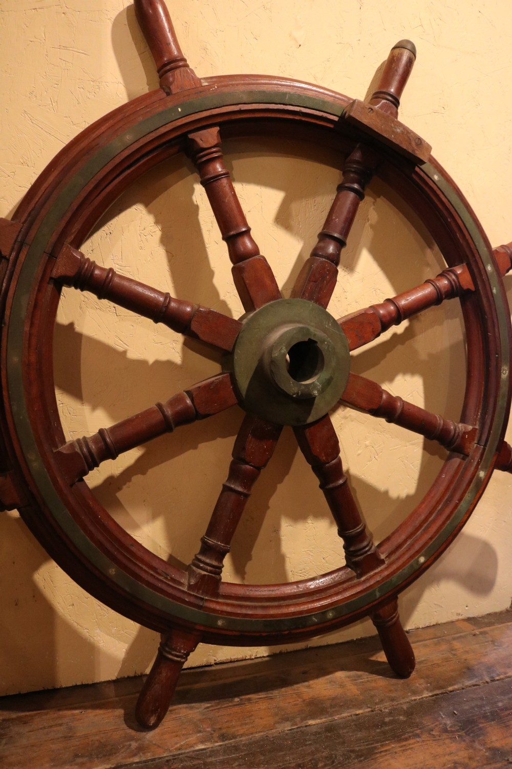 A Victorian wooden ships wheel featuring eight turned spokes, a central brass boss, and outer brass rim reinforcement. View III