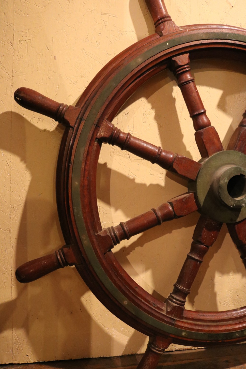 A Victorian wooden ships wheel featuring eight turned spokes, a central brass boss, and outer brass rim reinforcement. View V